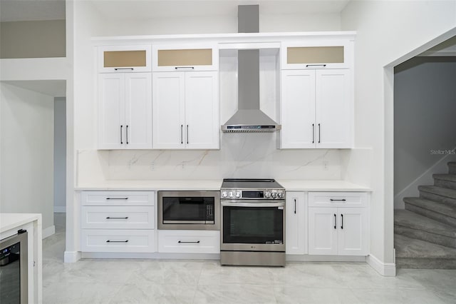 kitchen featuring appliances with stainless steel finishes, wall chimney range hood, and white cabinets