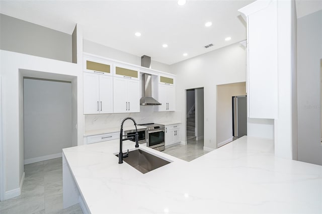 kitchen with wall chimney exhaust hood, stainless steel range with electric stovetop, white cabinets, light stone counters, and tasteful backsplash