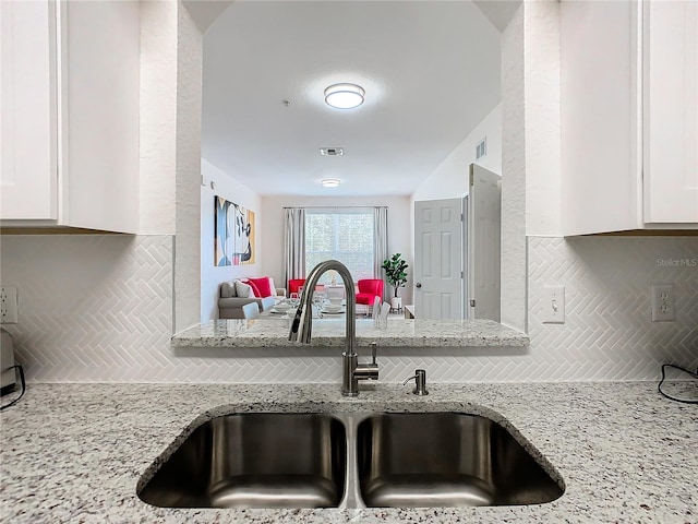 kitchen featuring light stone countertops, sink, decorative backsplash, and white cabinets