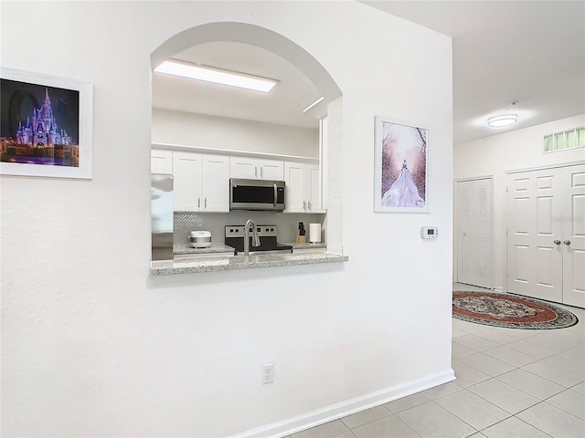 kitchen with white cabinets, light stone counters, stainless steel appliances, and light tile patterned flooring