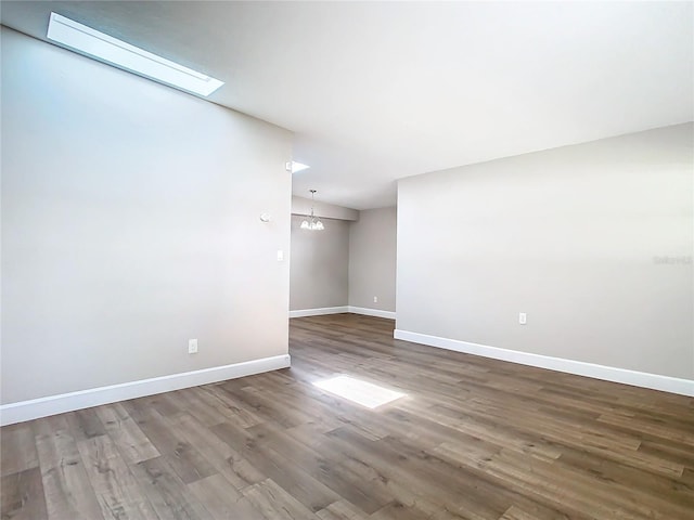 empty room featuring an inviting chandelier, wood-type flooring, and a skylight