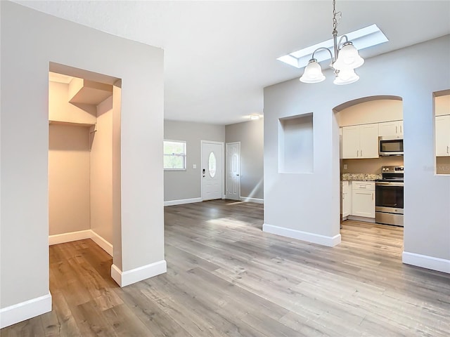 interior space featuring light wood-type flooring, hanging light fixtures, stainless steel appliances, white cabinets, and a chandelier