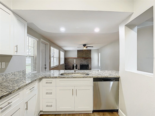 kitchen featuring stainless steel dishwasher, sink, white cabinets, and light stone counters