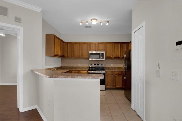 kitchen featuring stainless steel appliances, kitchen peninsula, decorative backsplash, and light tile patterned floors