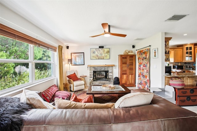 living room with a stone fireplace, light tile patterned floors, and ceiling fan