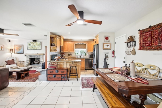 dining room featuring ceiling fan, a stone fireplace, and light tile patterned floors