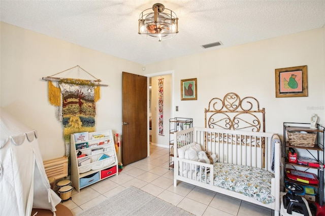 bedroom featuring a textured ceiling, a crib, and light tile patterned floors