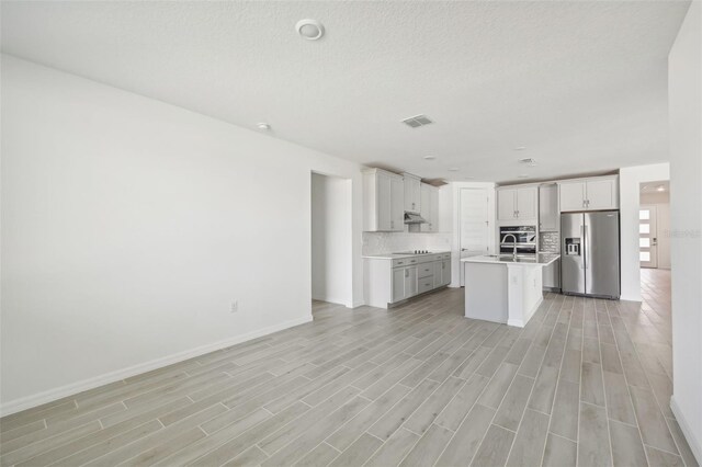 kitchen featuring stainless steel fridge, backsplash, sink, a center island with sink, and electric cooktop