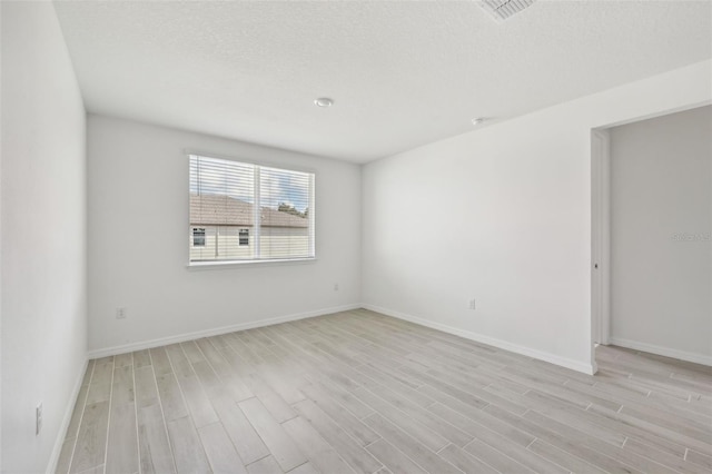 spare room with light wood-type flooring and a textured ceiling