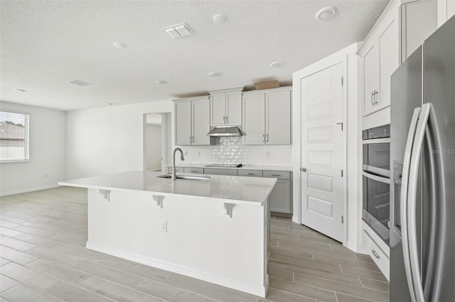 kitchen with tasteful backsplash, a breakfast bar, stainless steel appliances, a kitchen island with sink, and sink