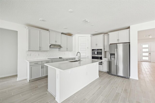 kitchen featuring black electric stovetop, double oven, sink, stainless steel fridge with ice dispenser, and an island with sink