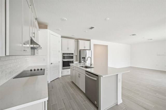 kitchen with white cabinetry, sink, stainless steel appliances, backsplash, and a kitchen island with sink