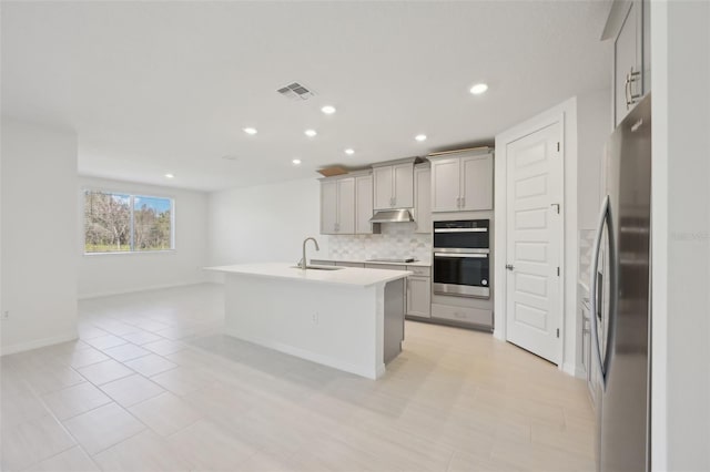 kitchen featuring decorative backsplash, appliances with stainless steel finishes, gray cabinets, and a center island with sink