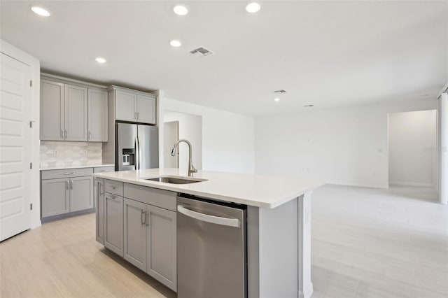 kitchen with gray cabinetry, stainless steel appliances, a center island with sink, and sink