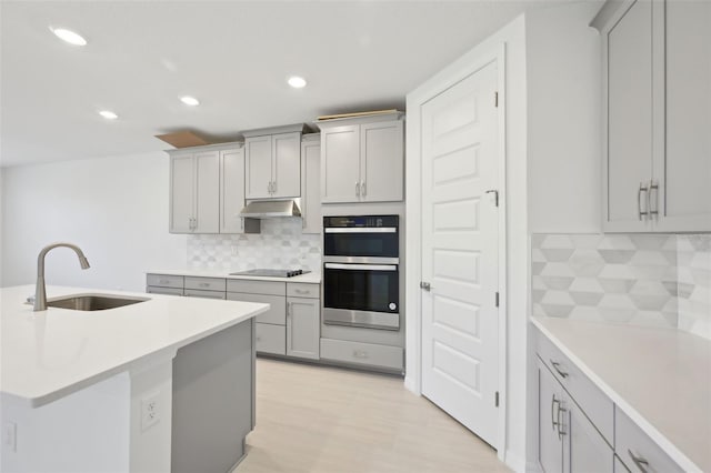 kitchen featuring decorative backsplash, gray cabinetry, stainless steel double oven, black electric cooktop, and sink