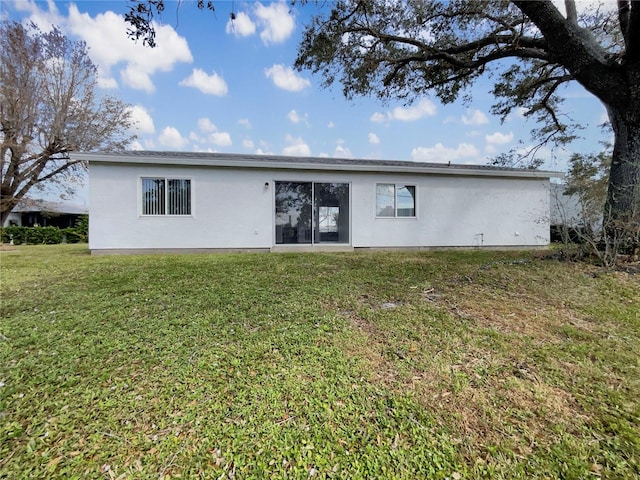back of property with stucco siding and a yard