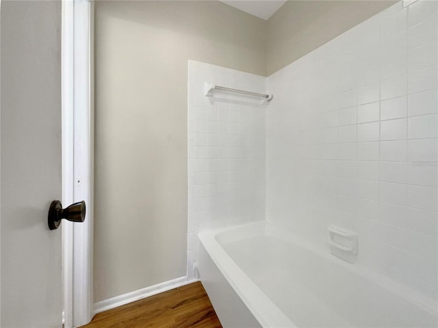 bathroom featuring baseboards, washtub / shower combination, and wood finished floors