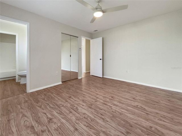 unfurnished bedroom featuring a closet, ensuite bath, wood-type flooring, and ceiling fan