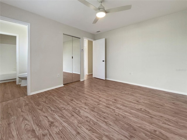 unfurnished bedroom with ceiling fan, baseboards, ensuite bathroom, and wood finished floors
