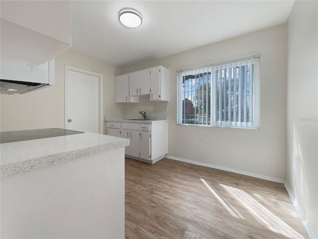 kitchen featuring light wood-type flooring, a sink, baseboards, white cabinets, and black electric stovetop