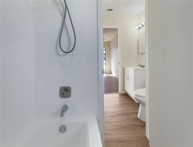full bath with visible vents, wood finished floors, shower / washtub combination, vanity, and toilet