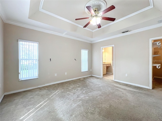 unfurnished bedroom featuring light colored carpet, ensuite bath, a raised ceiling, and a walk in closet