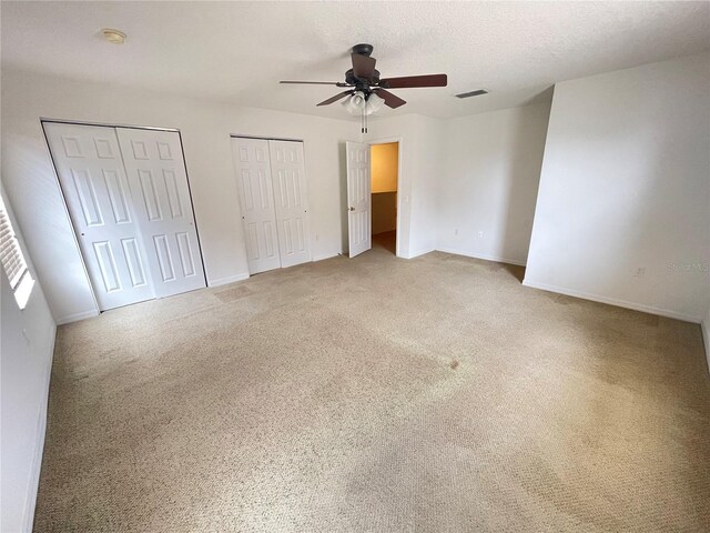 unfurnished bedroom featuring a textured ceiling, ceiling fan, two closets, and carpet floors