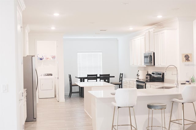 kitchen with sink, stainless steel appliances, kitchen peninsula, washer / clothes dryer, and white cabinets