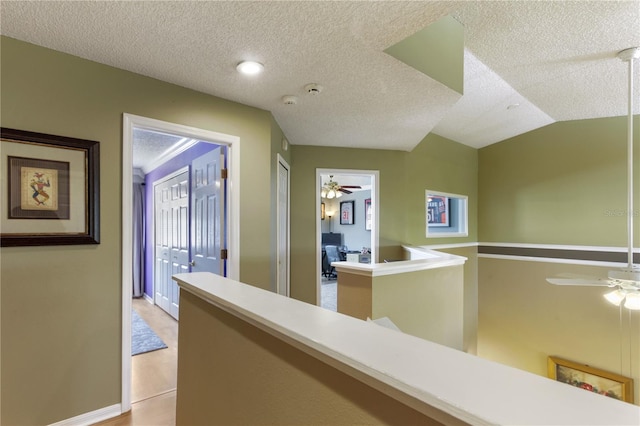 hall with a textured ceiling, vaulted ceiling, and light wood-type flooring