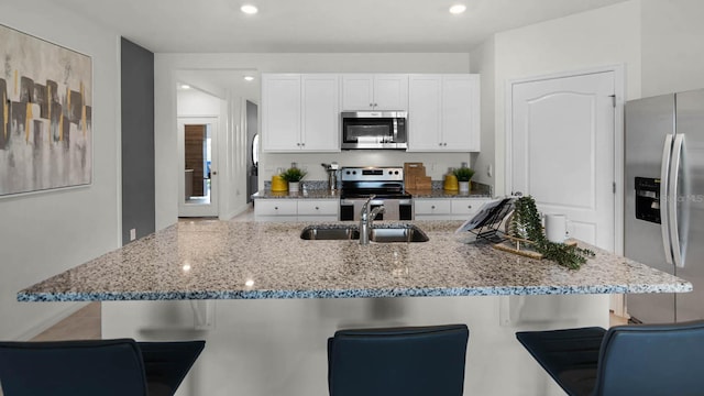 kitchen with appliances with stainless steel finishes, sink, white cabinetry, light stone counters, and a breakfast bar