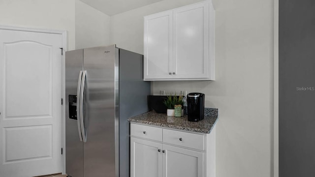 kitchen featuring stainless steel fridge, white cabinets, and dark stone counters