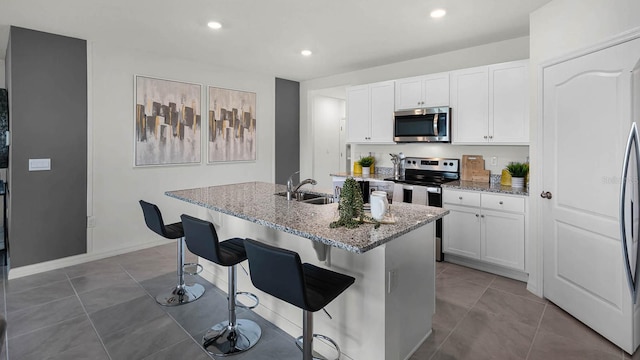 kitchen with white cabinets, light stone countertops, stainless steel appliances, and an island with sink