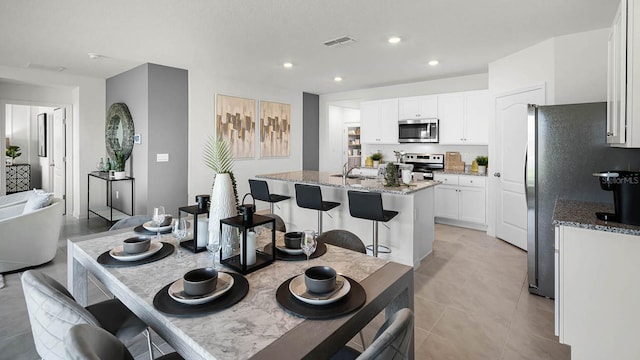 kitchen featuring a kitchen island with sink, stainless steel appliances, light stone countertops, and white cabinets