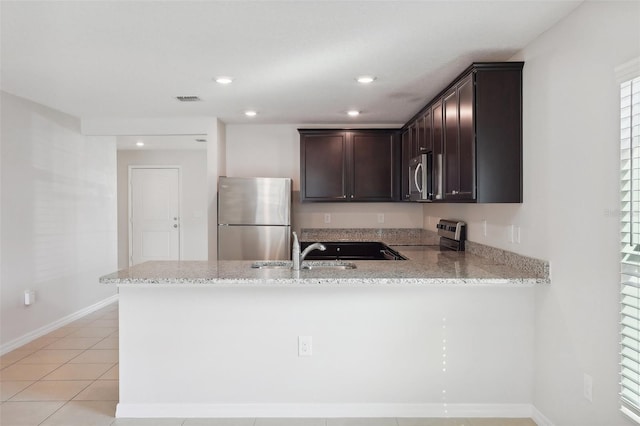 kitchen with kitchen peninsula, light stone countertops, stainless steel appliances, sink, and light tile patterned floors