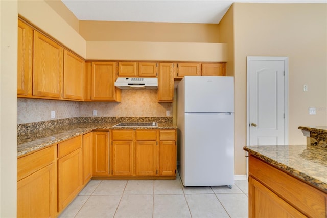 kitchen featuring black electric stovetop, light tile patterned floors, white refrigerator, and stone countertops