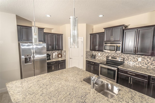 kitchen with sink, pendant lighting, light stone counters, and stainless steel appliances