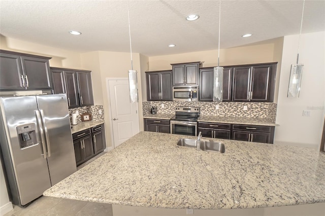 kitchen with stainless steel appliances, sink, pendant lighting, and a kitchen island with sink