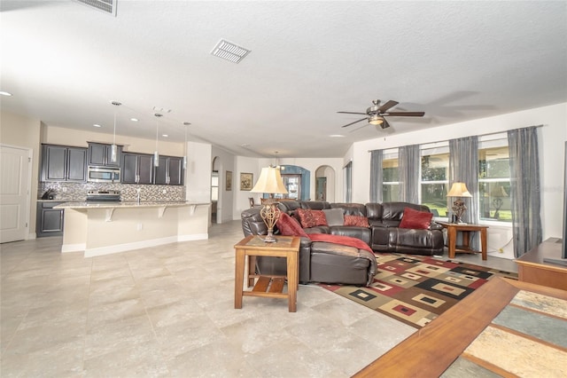 living room featuring ceiling fan, a textured ceiling, sink, and light tile patterned floors