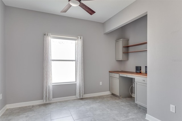 interior space with built in desk, light tile patterned floors, and ceiling fan