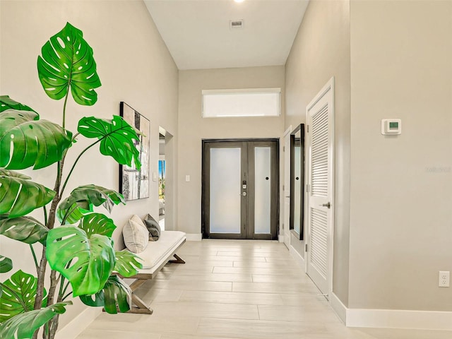 hallway with a towering ceiling, french doors, and light wood-type flooring