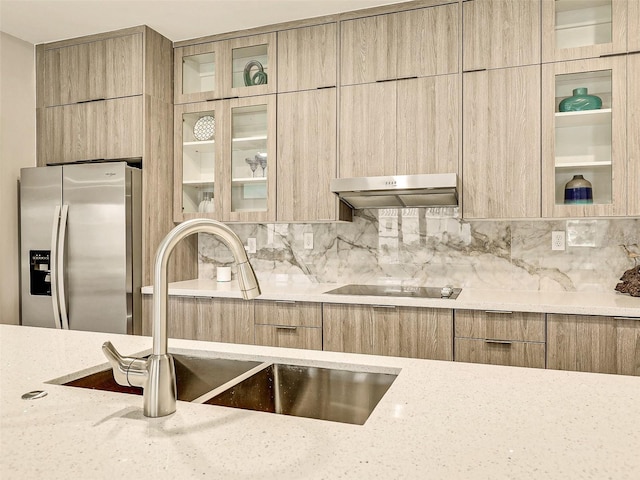 kitchen featuring light stone countertops, sink, black electric cooktop, exhaust hood, and stainless steel refrigerator with ice dispenser