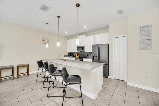 kitchen featuring appliances with stainless steel finishes, an island with sink, a kitchen breakfast bar, decorative light fixtures, and white cabinets