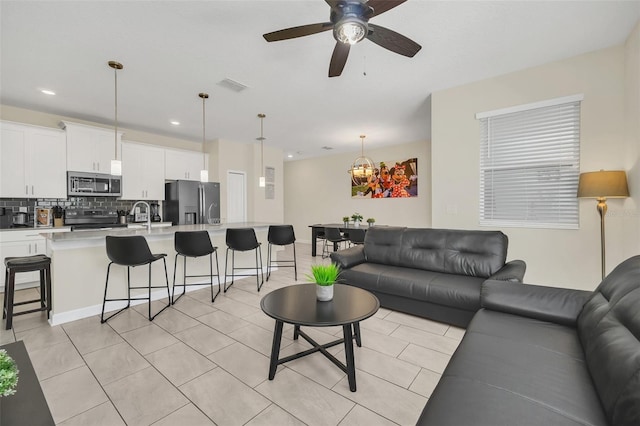 living room featuring sink, light tile patterned flooring, and ceiling fan with notable chandelier