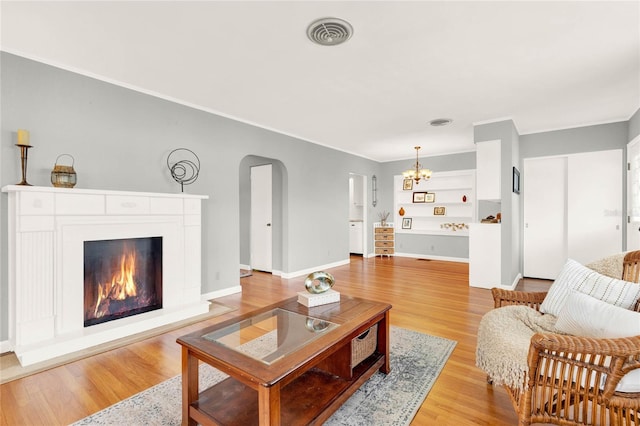 504 Osceola Ave, Eustis, FL 32726 - living room with arched walkways, a chandelier, light wood-style flooring, a warm lit fireplace, and ornamental molding