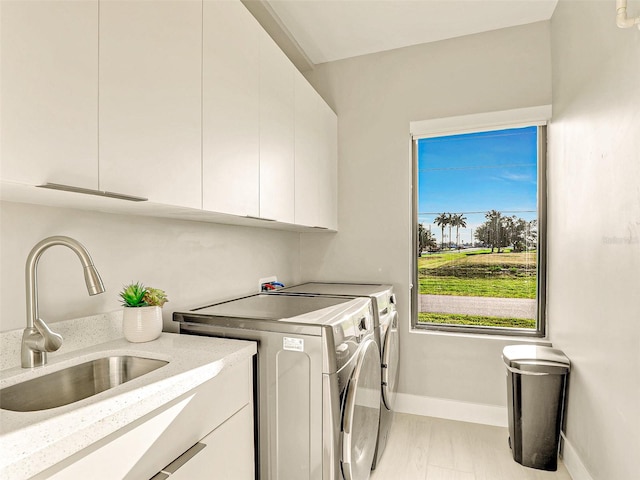 clothes washing area with sink, light hardwood / wood-style flooring, cabinets, and washing machine and clothes dryer