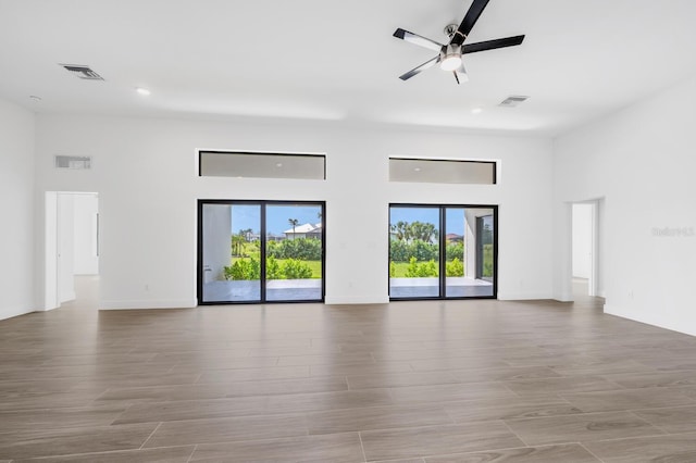 empty room featuring a towering ceiling, ceiling fan, and light wood-type flooring