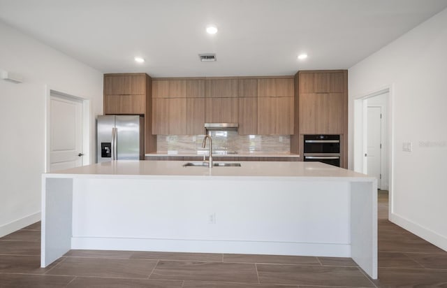 kitchen featuring sink, decorative backsplash, a spacious island, and stainless steel refrigerator with ice dispenser