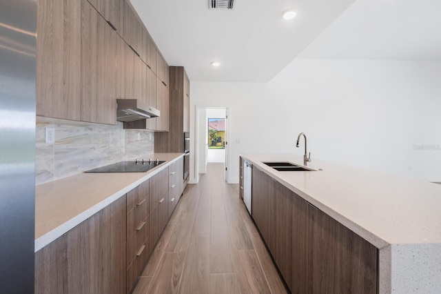 kitchen with black electric cooktop, sink, decorative backsplash, and a kitchen island with sink