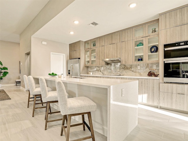 kitchen with extractor fan, appliances with stainless steel finishes, a kitchen bar, and a large island with sink