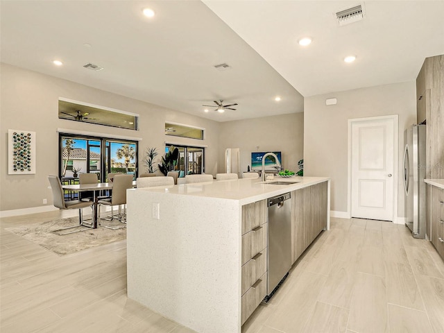 kitchen featuring an island with sink, sink, light wood-type flooring, appliances with stainless steel finishes, and ceiling fan